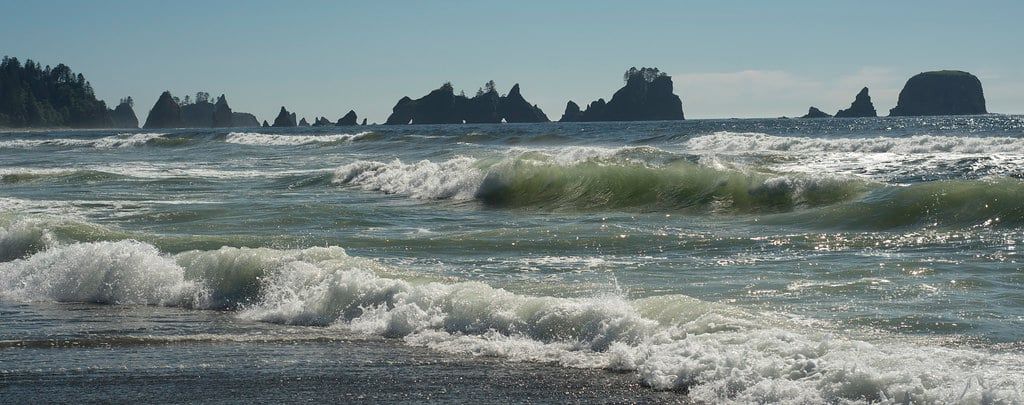 Breaking ocean waves roll toward Shi Shi Beach with the sea stacks of Point of Arches silhouetted on the horizon in Olympic National Park.