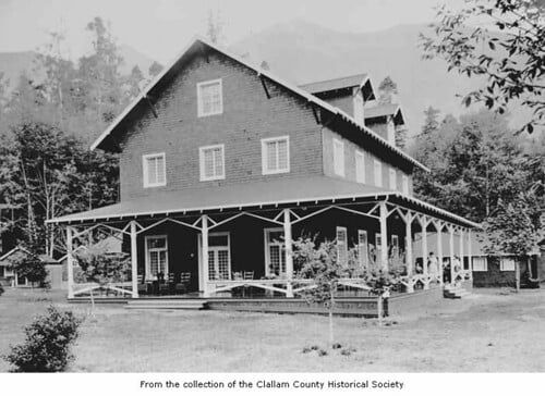Historic black-and-white photograph of Lake Crescent Lodge, originally known as Lake Crescent Tavern, showing its wraparound covered porch and lawn in Olympic National Park.
