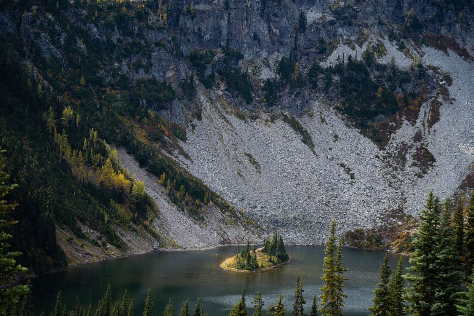 An elevated view of Lake Ann and its small island surrounded by talus slopes and autumn foliage along the Maple Pass Loop in the North Cascades.