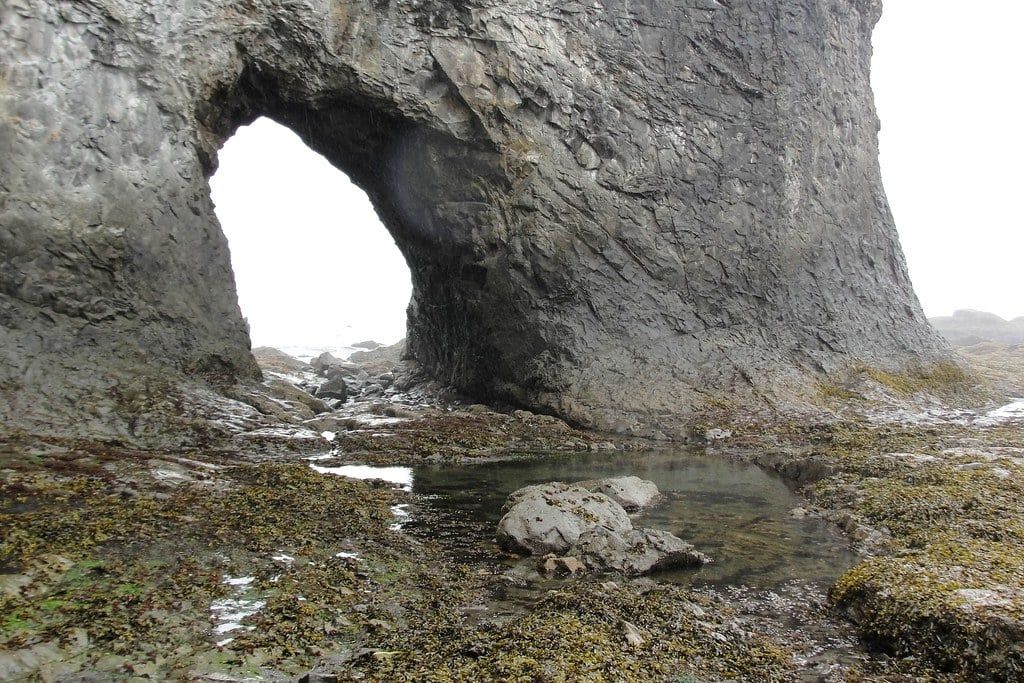 A natural rock arch known as Hole-in-the-Wall stands above rocky tide pools on Rialto Beach in Olympic National Park.