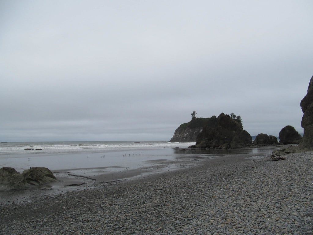 Rocky sea stacks and Abbey Island stand along the cobble shoreline and surf at Ruby Beach in Olympic National Park.