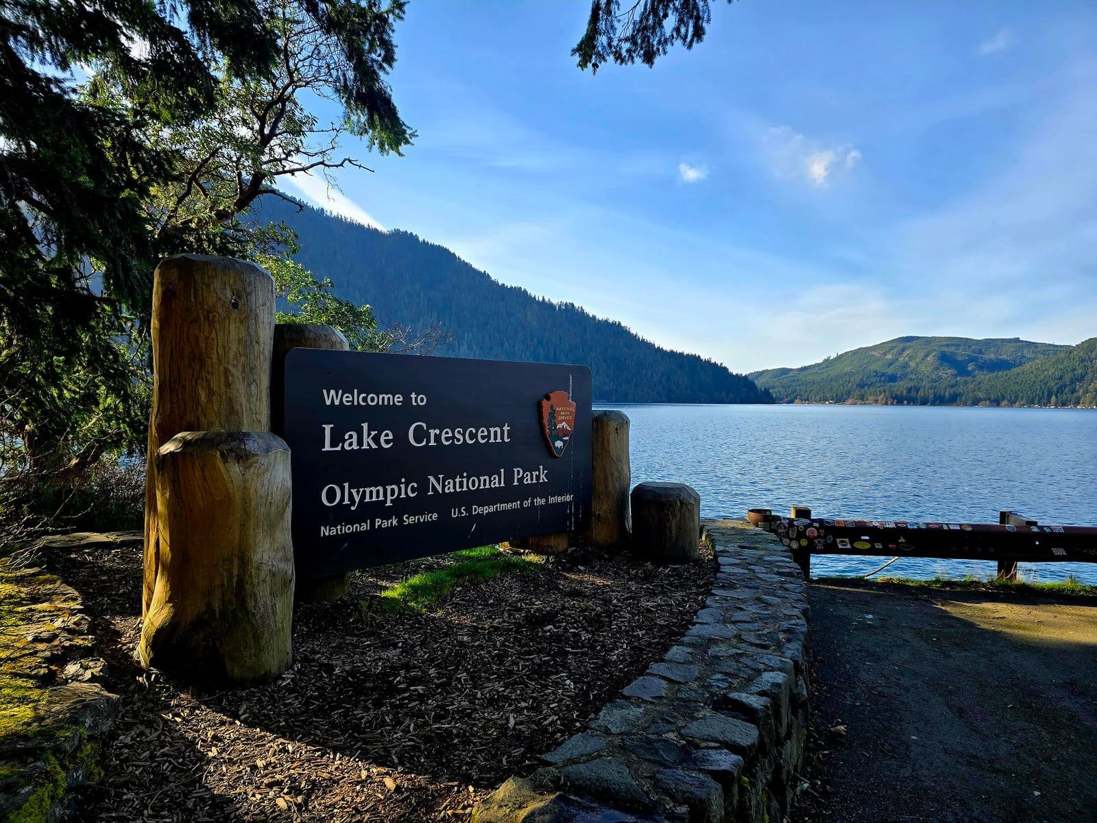 A National Park Service welcome sign overlooks Lake Crescent and forested mountains in Olympic National Park.